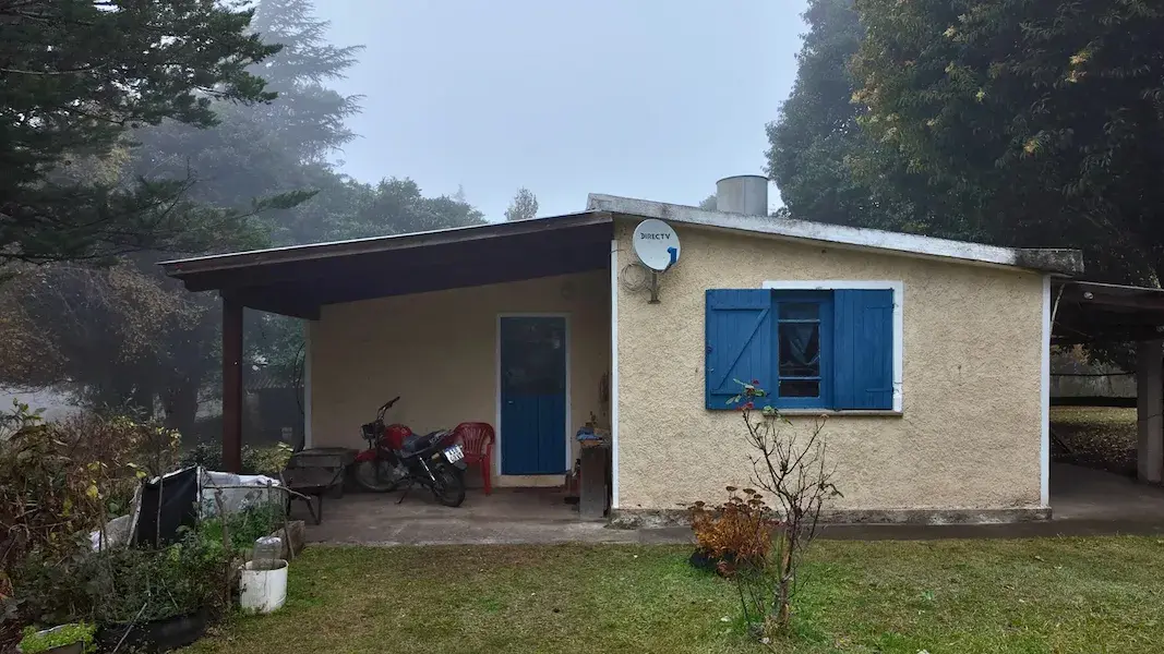 Frente de casa de 2 dormitorios con galería y puerta azul en venta en Athos Pampa, Valle de Calamuchita