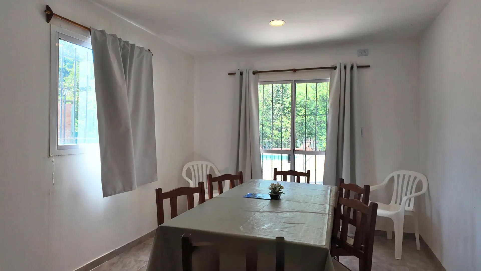 Comedor luminoso con mesa y sillas y ventanal con vista a la pileta en departamento de 2 dormitorios en Villa del Dique