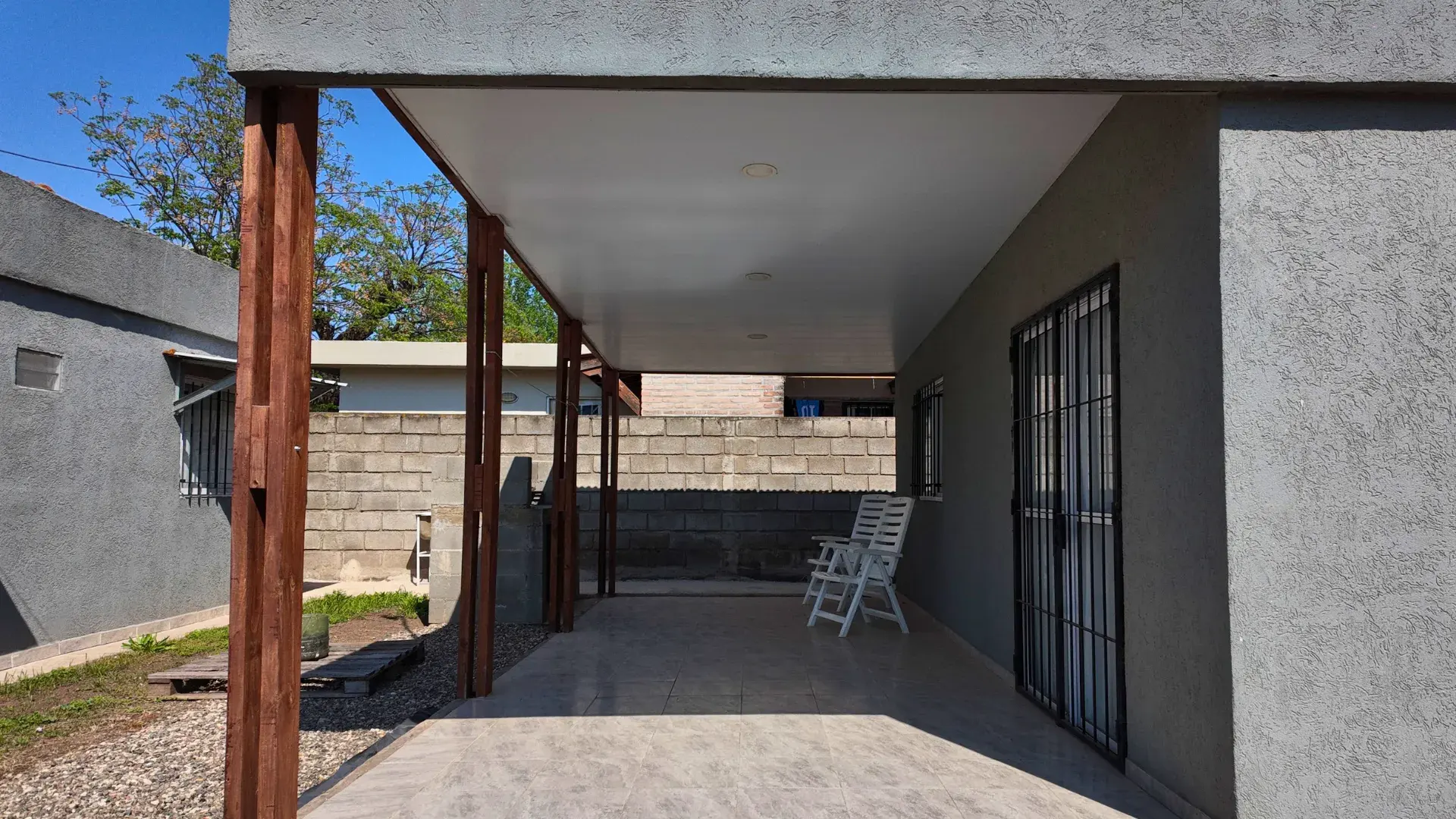 Galería con cochera semicubierta, columnas de madera y sillones de descanso en departamento en alquiler en Villa del Dique
